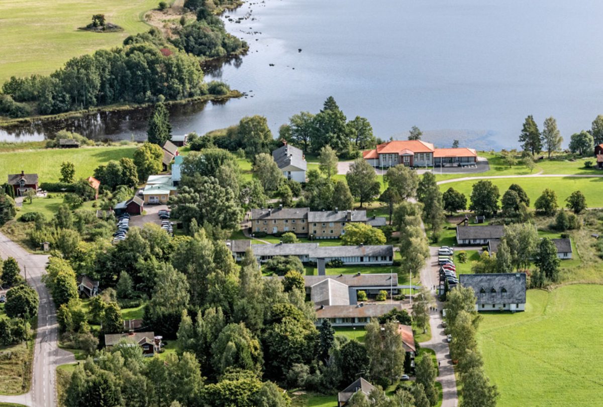 Flygbild över skolområdet. Lummigt och grönt, flertalet skolbyggnader omgivna av åkrar på tre sidor och sjö på den fjärde.