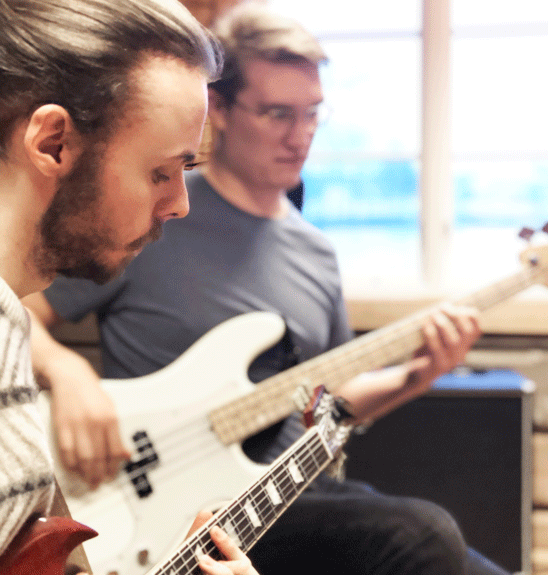 Två unga män spelar koncenterat på elgitarr och bas