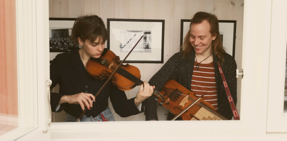 Två ungdomar sstår i ett fönster och spelar fiol och nyckelharpa