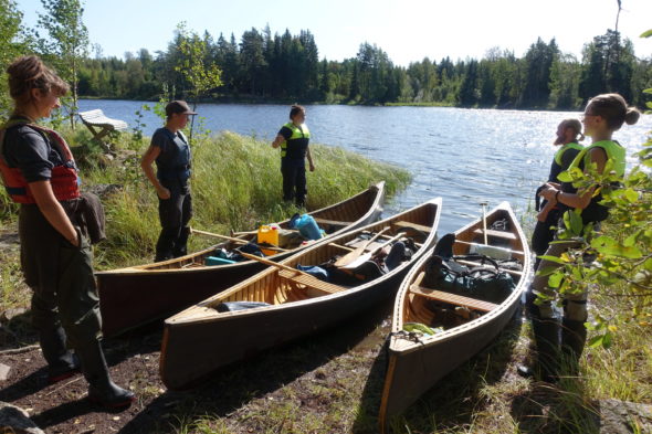 Ungdomar står runt tre kanoter som ligger uppdragna på land.