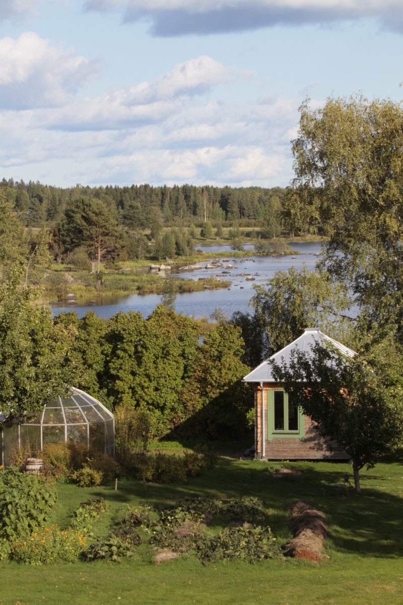 Ett växthus, odlingsbäddar och en liten timmerstuga med koniskt tak