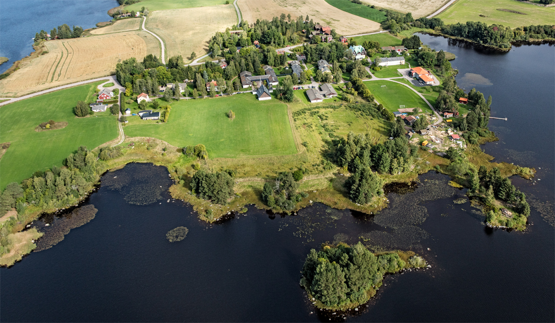 Flygbild över Sjöviks folkhögskola. Halva skolområdet omges av åkermark och halva omges av vatten.